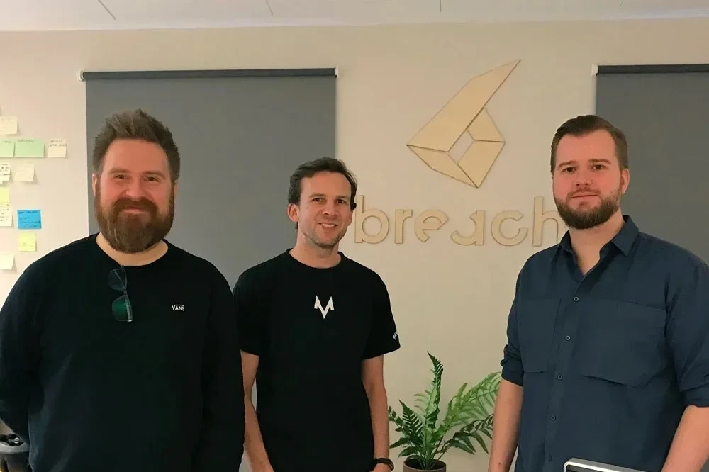 a photo of the three breach founders in front of a laser cut of the breach logo